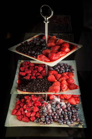 Assortment of frozen thawed berries served on three leveled plate against black background