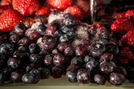 Closeup frozen thawed blueberries and red strawberries served on blue plate against black background