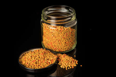 Fresh bee pollen grain in black cover next to small glass jar full of bee pollen over black backgroundの写真素材