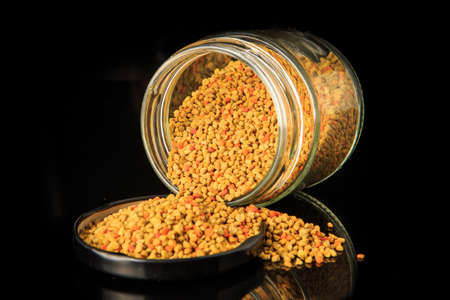 Closeup raw bee pollen grain in cover next to small glass jar full of bee pollen over black backgroundの写真素材