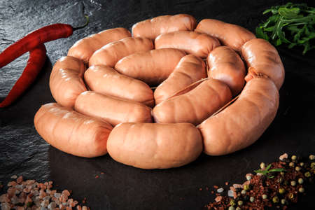 Circle set of raw short thick meat sausages served with pink salt, spices, rucola and red chili pepper on black backgroundの写真素材