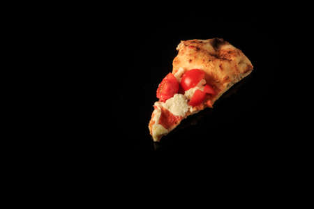 top view of single piece of pizza with sliced cherry tomatoes and mozzarella cheese pieces on black frosted backgroundの写真素材