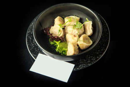 top view on boiled russian pelmeni with meat filling served with fresh salad in deep bowl with white visit card on topの写真素材