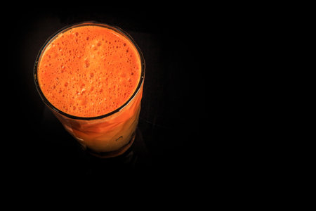 top view on tall faceted plastic glass of fresh orange carrot juice stands on black background