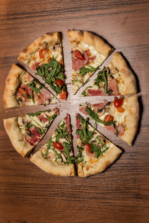vertical top view of sliced in eight pieces of pizza with arugula, ham, mushrooms and tomatoes on...