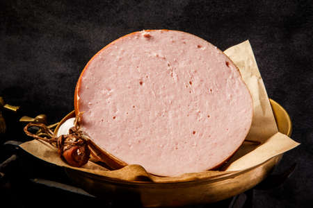 closeup big piece of meat boiled sausage bologna on piece of craft paper on antique scales over black backgroundの写真素材