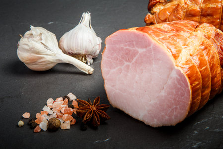 closeup chunk of smoked bacon with pink himalayan salt, aromatic spices and two whole garlic on...