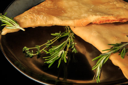 macro view of two fried caucasian chebureki on gray glossy restaurant plate decorated with green...