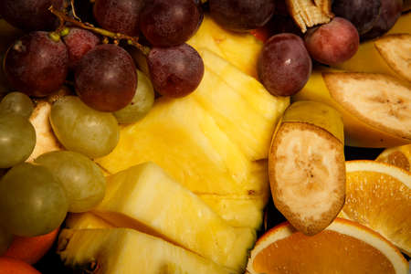 top view on sliced bananas, oranges, pineapples, and grapesの写真素材