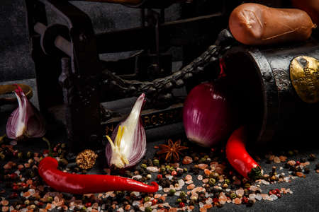 Closeup heap of spices, pink salt, chili pepper, sliced onion and raw wieners on antiquarian scales on black backgroundの写真素材
