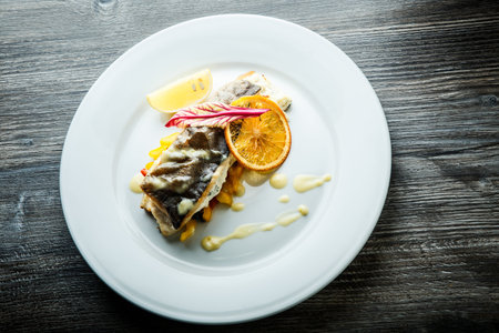 top view of roasted sea fish with white sauce served on pickled pepper garnish on round plate on...