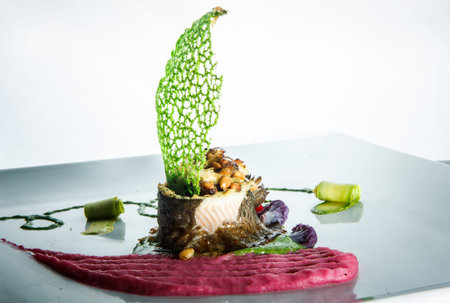 closeup stuffed sea fish served with pink puree and original decoration on plate against white...