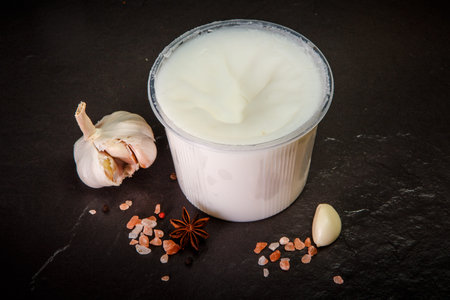 white lard spread in plastic bowl served with assorted spices, divided garlic and green basil leaf on black backgroundの写真素材