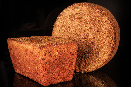 closeup two whole loaves of cereal bread with sesame seeds decoration served on black background