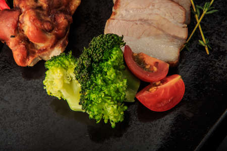 top view macro broccoli and tomatoes with smoked meat and chicken pieces with sauce on black restaurant plateの写真素材