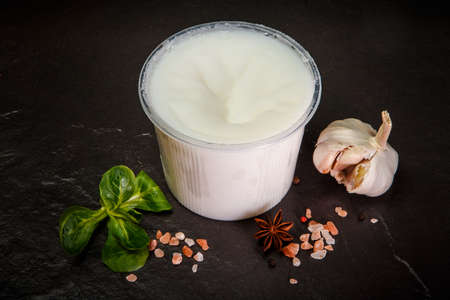 white cream lard spread in plastic bowl served with assorted spices, garlic and green basil leaf on black backgroundの写真素材