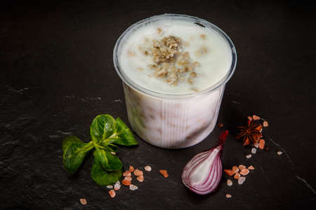 white lard spread in plastic bowl served with assorted spices, green basil leaf and red onion slice on black backgroundの写真素材