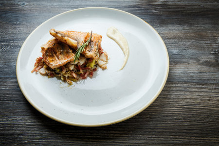 top view on grilled fish pieces decorated with rosemary served on meat salad on round white plate on...