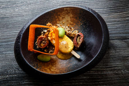 top view on restaurant fish dish with exclusive garnish decoration served in original black plate on wooden tableの写真素材