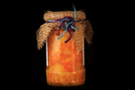 closeup single tall glass jar of delicious homemade fruit jam and rustic decoration served on black...
