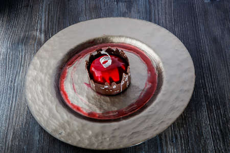 trendy red mirror glazed mousse cake in apple shape with caramel dressing on gold restaurant plate on wooden tableの写真素材
