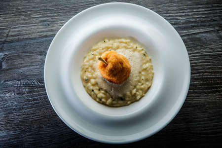 top view on boiled barley porridge decorated with breaded whole pear served in deep white restaurant plate on wooden tableの写真素材