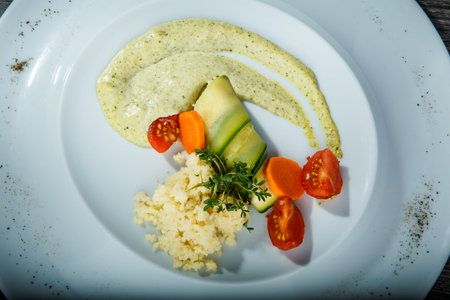 top view closeup rice and sliced vegetables originally decorated with green sauce and greens served in white restaurant plate on wooden tableの写真素材