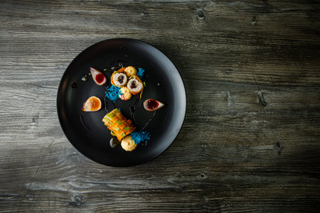 top view on exquisite decorated vegetable roll stuffed with minced meat with assorted sauces on black dish on wooden tableの写真素材