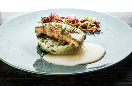 roasted sea fish with rice, sauce, mushrooms, and greens served on blue plate against white...
