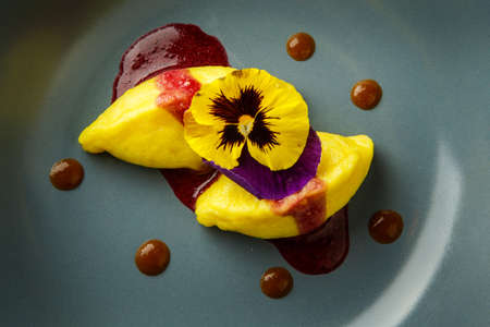 top view closeup two big yellow dumplings decorated with red sauce and fresh flower served on blue restaurant plateの写真素材