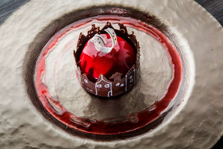 top view closeup red mirror glazed mousse cake in apple shape with chocolate decoration on gold plate on wooden tableの写真素材