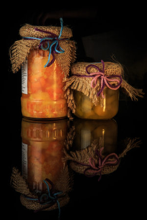 vertical view of two small glass jars of tasty homemade fruit and berry jam served on black...