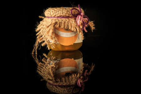 small glass jar of delicious homemade jam and rustic decoration served on black mirror background with reflectionの写真素材