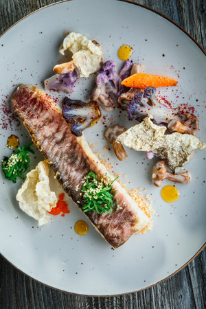 vertical view of exquisite decorated grilled fish fillet, mushrooms, and vegetables on white round...