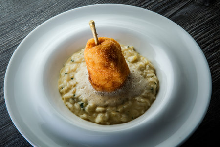 closeup boiled barley porridge decorated with breaded roasted whole pear served in deep white...
