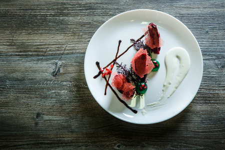 top view on exclusively decorated delicious restaurant dessert served on white plate on dark wooden table backgroundの写真素材
