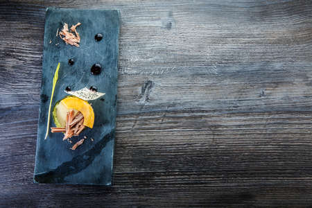 top view on exquisite dessert of baked avocado decorated with chocolate slices, cream sauce, and syrup served on black stone board on wooden tableの写真素材