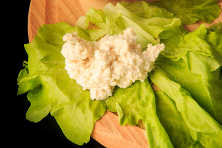 top view closeup small heap of homemade cottage cheese on green salad leaf served on round wooden boardの写真素材