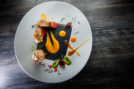 top view on exquisite restaurant dish of baked quail legs decorated with assorted sauces on round white plate on wooden tableの写真素材