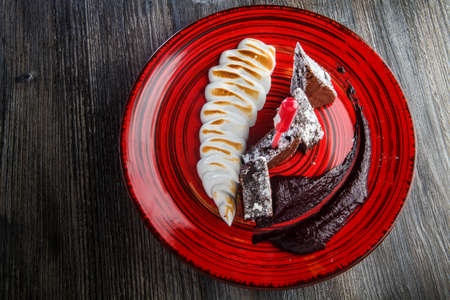 top view on sliced homemade brownie cake with baked white cream and chocolate sauce on restaurant plate on wooden tableの写真素材