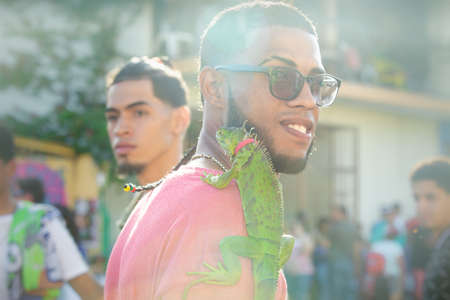 Concepcion De La Vega, DOMINICAN REPUBLIC - FEBRUARY 09, 2020: closeup portrait of dominican young man with green iguana on his shoulder on February 9 in Concepcion De La Vegaのeditorial素材