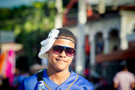 Concepcion De La Vega, DOMINICAN REPUBLIC - FEBRUARY 09, 2020: closeup young man in vendetta white mask and pink glasses walks by city street on February 9 in Concepcion De La Vegaのeditorial素材