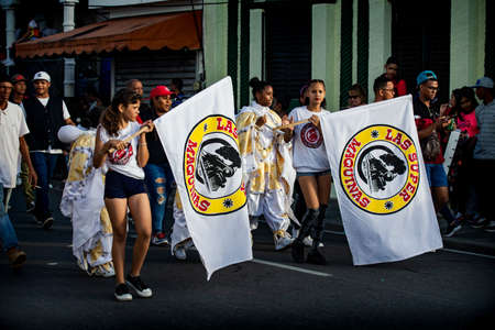 Concepcion De La Vega, DOMINICAN REPUBLIC - FEBRUARY 09, 2020: young women carry big flags with group emblem by city street at dominican carnival on February 9 in Concepcion De La Vegaのeditorial素材
