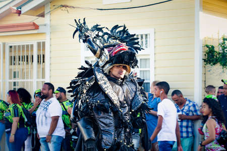 Concepcion De La Vega, DOMINICAN REPUBLIC - FEBRUARY 09, 2020: man in sparkling black costume walks by city street full of people at dominican carnival on February 9 in Concepcion De La Vegaのeditorial素材
