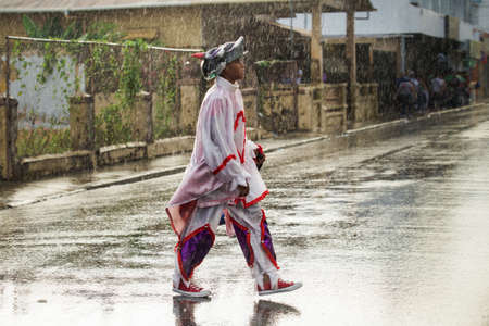 Concepcion De La Vega, DOMINICAN REPUBLIC - FEBRUARY 11, 2019: teenager in motley carnival costume walks under rain by dominican city street on February 11 in Concepcion De La Vegaのeditorial素材