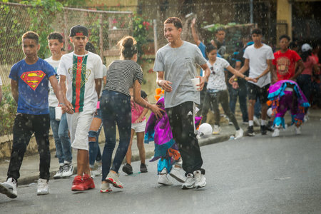 Concepcion De La Vega, DOMINICAN REPUBLIC - FEBRUARY 11, 2019: group of teenagers passes under tropical rain by city street at dominican carnival on February 11 in Concepcion De La Vegaのeditorial素材