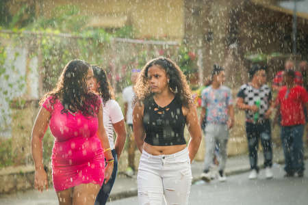 Concepcion De La Vega, DOMINICAN REPUBLIC - FEBRUARY 11, 2019: closeup young girls walk under tropical rain by city street at dominican carnival on February 11 in Concepcion De La Vegaのeditorial素材