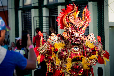 Concepcion De La Vega, DOMINICAN REPUBLIC - FEBRUARY 09, 2020: people take photos of man in vivid costume passing by city street at dominican carnival on February 9 in Concepcion De La Vegaのeditorial素材