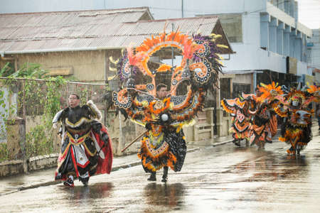 Concepcion De La Vega, DOMINICAN REPUBLIC - FEBRUARY 11, 2019: people in original costumes walk under rain by city street at dominican carnival on February 11 in Concepcion De La Vegaのeditorial素材
