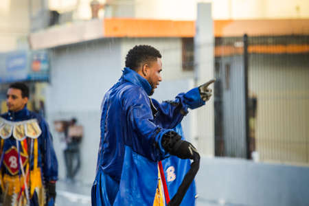 people in shiny blue costumes pass by under tropical rain at dominican carnivalのeditorial素材